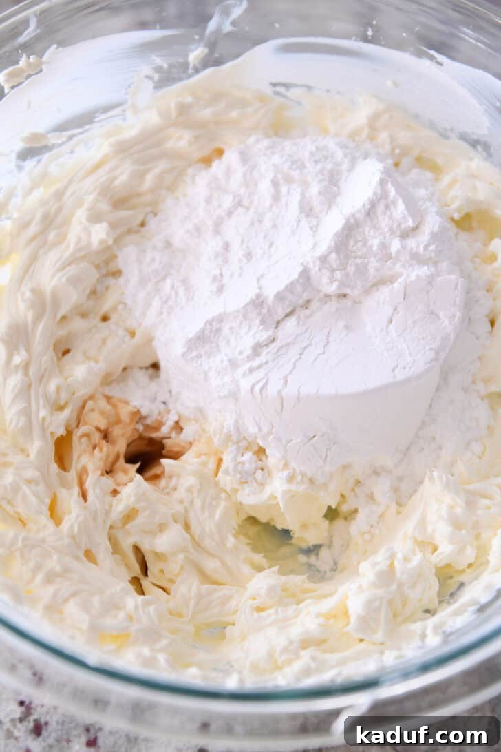 Ultimate No-Bake Cheesecake 3 Top down view of whipped cream cheese with powdered sugar on top in a clear glass bowl, ready for mixing.