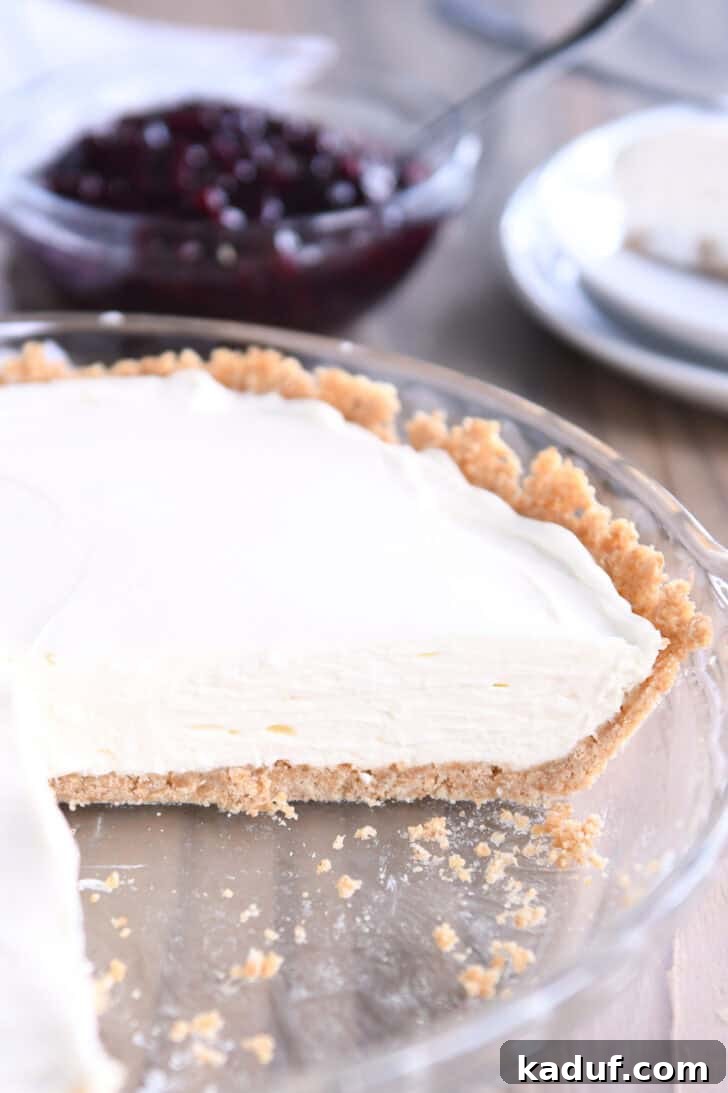 Ultimate No-Bake Cheesecake 8 A beautifully set no-bake cheesecake with a golden graham cracker crust, still in its clear glass dish. A large, perfect slice has been carefully removed from the center, showcasing its creamy texture.