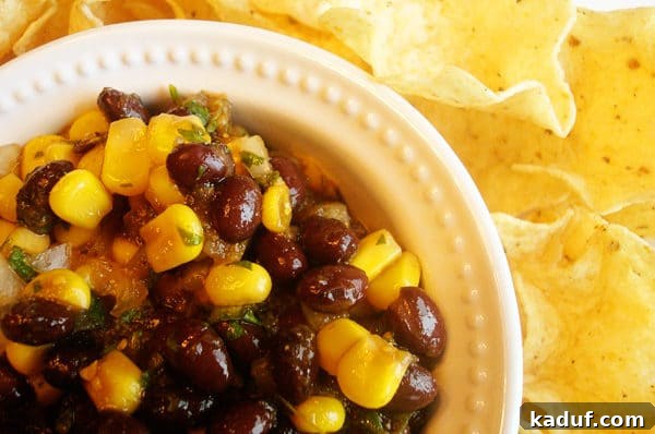 Tangy Balsamic Black Bean Fiesta 3 A white bowl brimming with black bean and corn salsa, perfectly paired with a handful of crunchy tortilla chips.