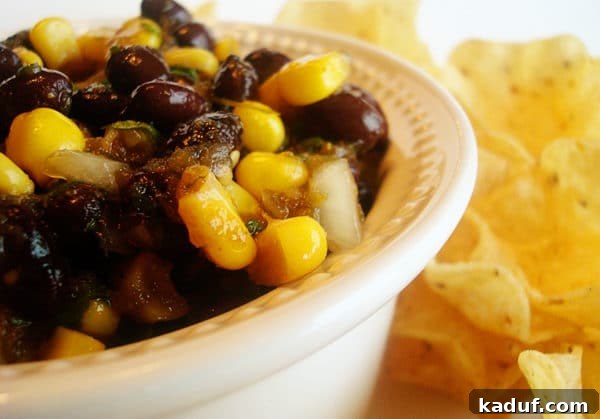 Tangy Balsamic Black Bean Fiesta 5 A vibrant serving of corn and black bean salsa on a plate, surrounded by crispy tortilla chips, inviting a delicious dip.