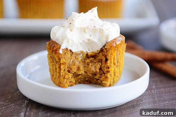 Pure Pumpkin Pie Cup Delights 3 A crustless pumpkin pie cupcake on a white plate with a bite taken out, showing its creamy texture, topped with a dollop of whipped cream.