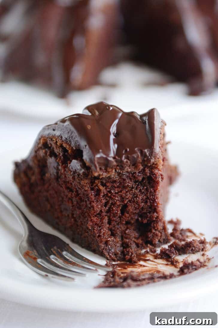 Velvet Chocolate Fudge Bundt 8 A delicious slice of chocolate bundt cake, revealing its moist and fudgy interior, with a bite taken out, gracefully resting on a pristine white plate.