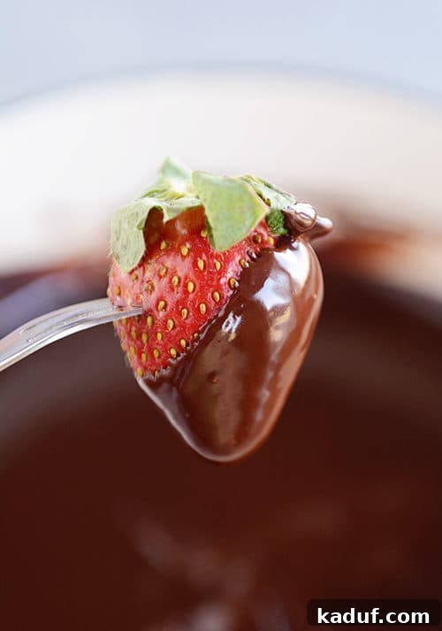 Decadent Chocolate Fondue 12 A fork holding a strawberry half dipped in chocolate fondue, poised over a pot of luscious chocolate fondue.