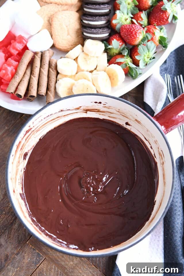 Decadent Chocolate Fondue 6 A pot of rich chocolate fondue surrounded by a white tray filled with bananas and strawberries, ready for dipping.