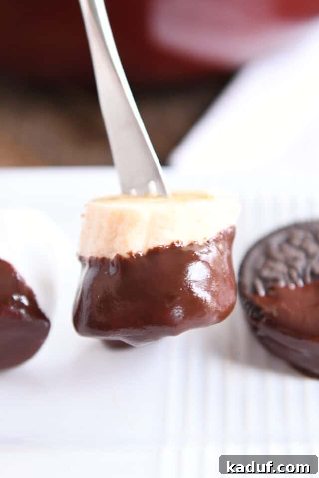 Decadent Chocolate Fondue 10 A banana slice beautifully dipped in chocolate, resting on a pristine white tray.