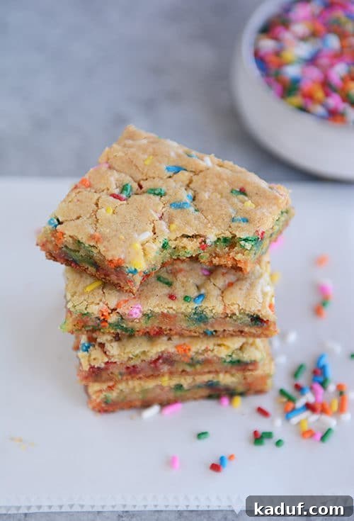 Ultimate Chewy Funfetti Blondies 2 Stacked thin and chewy funfetti blondie bars, with a bite taken out of the top one, showcasing colorful sprinkles.