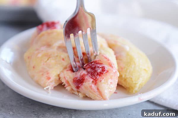 Overnight Strawberry Cheesecake Rolls 3 A strawberry cream cheese roll on a plate with one bite cut out on a fork ready to eat.