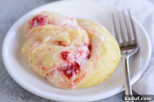 Overnight Strawberry Cheesecake Rolls 4 A strawberry cream cheese roll on a white plate, with a fork laying next to it.