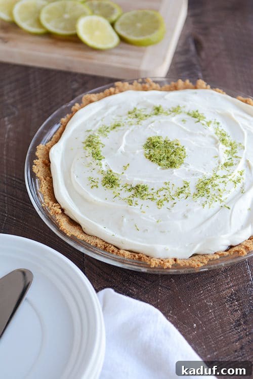 Decadent Key Lime White Chocolate Cheesecake 3 A stunning whole Key Lime White Chocolate Cheesecake Pie, elegantly topped with delicate white chocolate shavings and a sprinkle of fresh lime zest, resting on a rustic wooden surface.