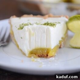 A vibrant Key Lime White Chocolate Cheesecake Pie slice on a plate, garnished with lime zest and a hint of white chocolate.