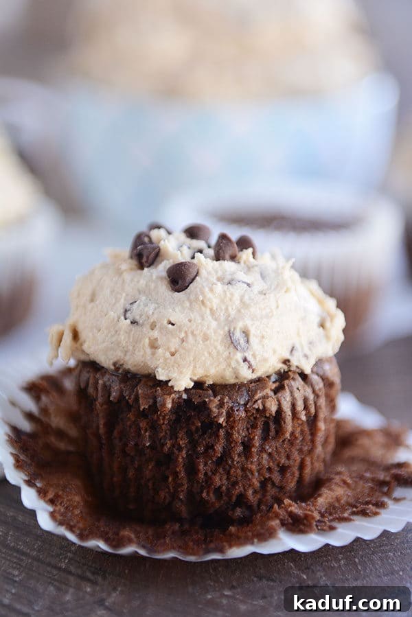 Decadent Fudge Brownie Cupcakes 2 An unwrapped chocolate brownie cupcake generously topped with a thick layer of creamy cookie dough frosting, ready to be enjoyed.