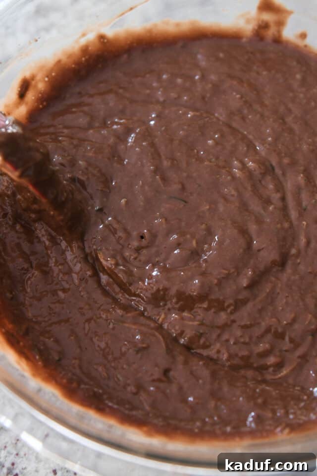 Ultimate Chocolate Zucchini Indulgence 5 A rubber spatula stirring rich chocolate zucchini cake batter in a mixing bowl, illustrating the gentle mixing technique.