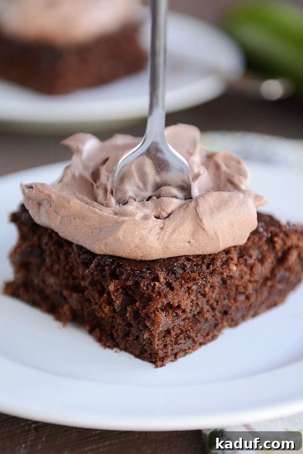 Ultimate Chocolate Zucchini Indulgence 7 A fork piercing a slice of moist chocolate zucchini cake, generously topped with fluffy whipped chocolate frosting, highlighting its tempting texture.