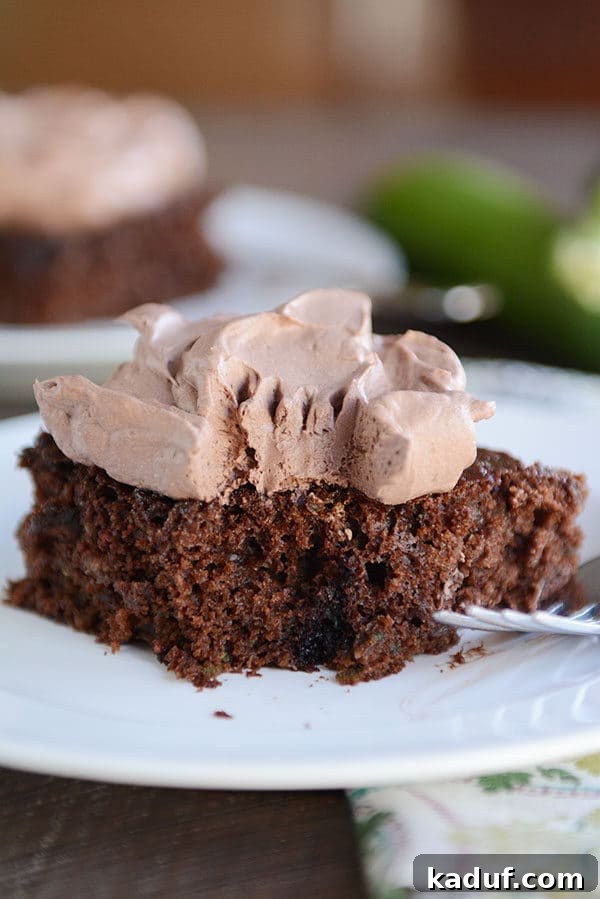 Ultimate Chocolate Zucchini Indulgence 8 A slice of rich chocolate zucchini cake with a bite taken out, revealing the moist interior and topped with creamy chocolate whipped frosting.