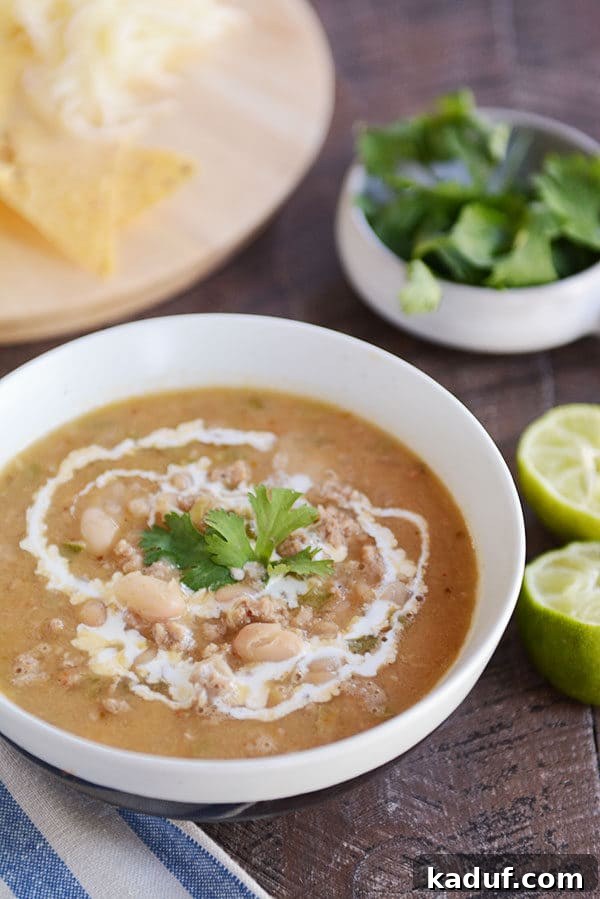 Deep Roasted Garlic White Bean Chili 2 A white bowl of white bean chili with a swirl of cream and parsley on top.