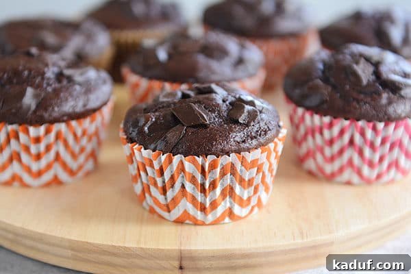 Fudgy Double Chocolate Chunk Muffins 5 Four freshly baked double chocolate chunk muffins in colorful paper liners, arranged neatly.