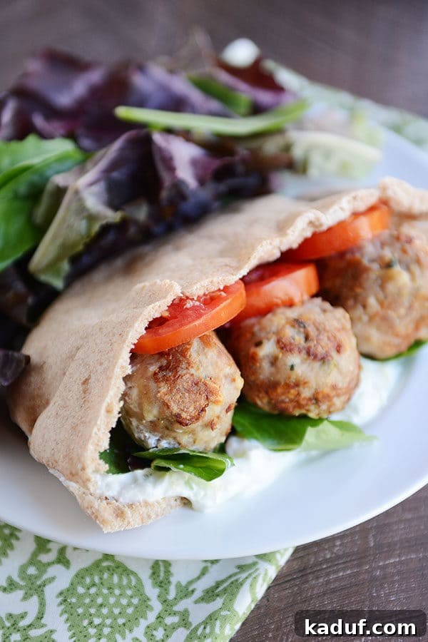 Hearty Greek Meatball Pockets with Quick Tzatziki 2 A meatball and veggie stuffed Greek pita next to a large serving of lettuce on a white plate.