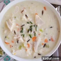A white bowl full of creamy chicken and wild rice soup, garnished with fresh chives, ready to be served.