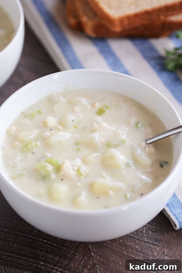 Our Signature New England Clam Chowder 4 A pristine white bowl of New England clam chowder with a spoon resting inside, ready to be enjoyed.