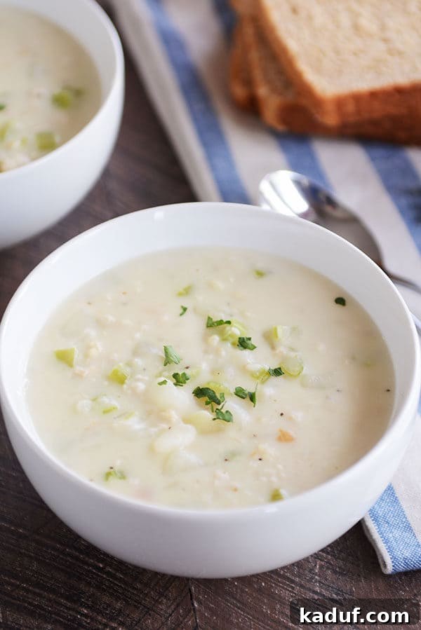 Our Signature New England Clam Chowder 5 A white bowl of New England clam chowder garnished with fresh parsley, ready to be served.