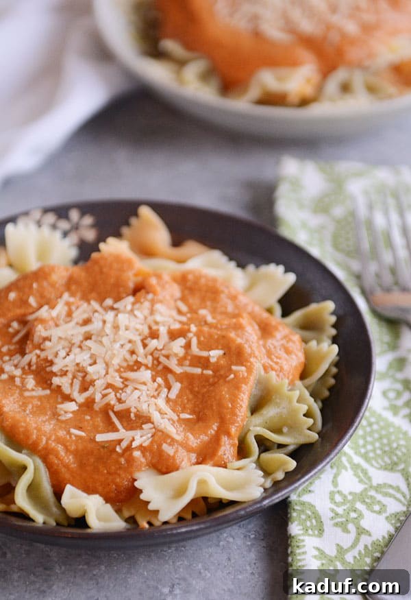 A beautiful bowl of cooked bowtie pasta generously topped with a rich, creamy harvest sauce and grated Parmesan cheese, embodying the warmth of fall.
