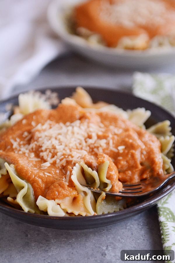 Close-up of a dark bowl filled with bowtie pasta and a generous serving of Trader Joe's copycat harvest pasta sauce, garnished with fresh Parmesan cheese.