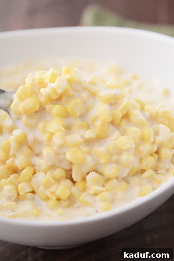Creamy Parmesan Corn Delight 3 A spoon taking a large scoop of creamy Parmesan cream corn out of a white oval bowl, showcasing its rich texture.