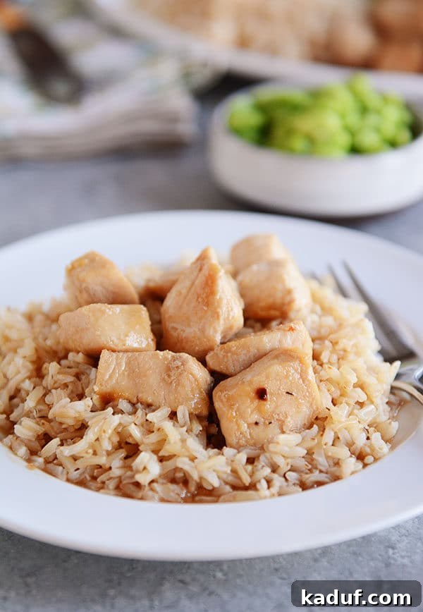 Effortless 20-Minute Skillet Honey Garlic Chicken 3 A white plate of cooked brown rice topped with golden brown honey garlic chicken cubes.