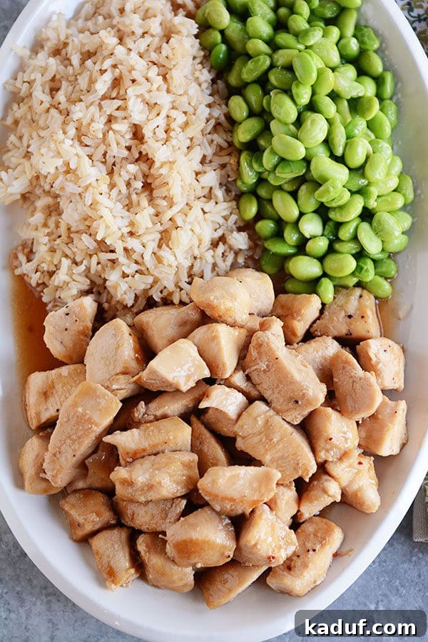 Effortless 20-Minute Skillet Honey Garlic Chicken 5 A large white oval platter with cooked honey garlic chicken, vibrant green edamame, and fluffy brown rice.