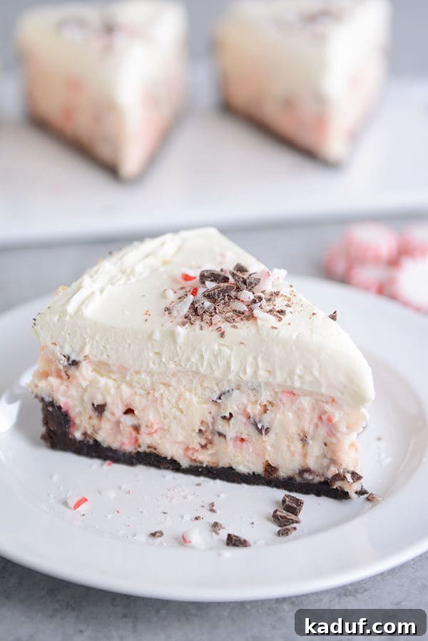 White Chocolate Mousse Cheesecake with Peppermint Bark 2 A slice of layered white chocolate peppermint cheesecake on a white plate, showcasing its rich layers and creamy texture.