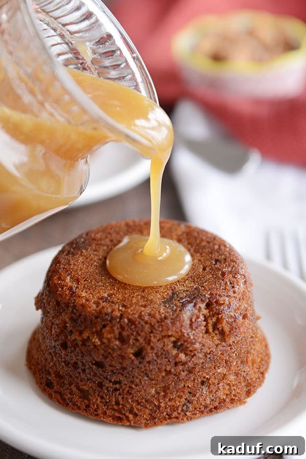 Gloriously Sticky Toffee Pudding Cake 2 A small cake on a white plate, with sticky toffee sauce being poured over the top. Golden, rich sauce cascades over a moist date cake, creating an inviting presentation.