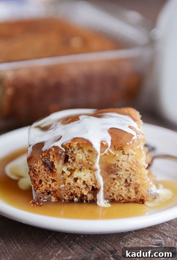 Gloriously Sticky Toffee Pudding Cake 5 A piece of sticky toffee pudding cake with light brown sauce and cream around and on top of the cake. The presentation is elegant and inviting.