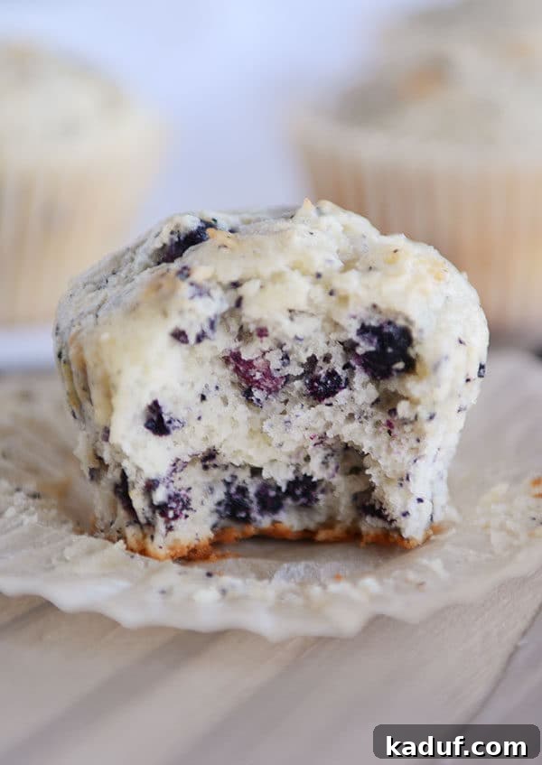 An unwrapped blueberry cream cheese muffin with a small bite taken out, revealing its soft interior and plump blueberries.
