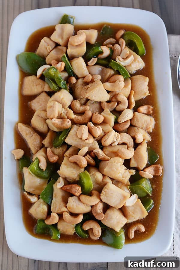Easy 30-Minute Cashew Chicken 2 Top down view of a large white platter of homemade Chinese cashew chicken with sauce and green peppers, garnished with fresh herbs.
