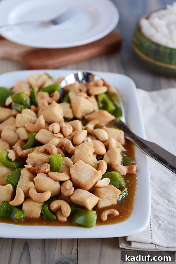 Easy 30-Minute Cashew Chicken 4 A large metal spoon scoops up saucy Chinese cashew chicken from a white tray, showcasing the tender chicken pieces and cashews.