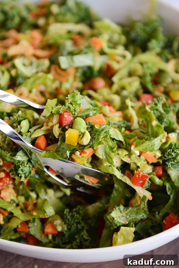 Honey Garlic Thai Chop 4 Metal tongs serving a generous scoop of chopped Thai salad from a large white bowl.
