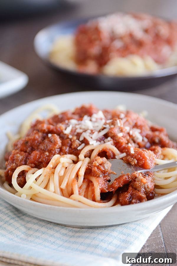 Whip Up a Quick Homemade Spaghetti Sauce Tonight 2 A fork twirling a bite of spaghetti noodles in a white bowl, generously topped with meaty spaghetti sauce and a sprinkle of Parmesan cheese, ready to be enjoyed.