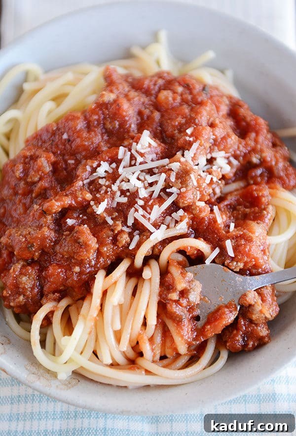Whip Up a Quick Homemade Spaghetti Sauce Tonight 5 A fork lifts a generous bite of spaghetti noodles from a white bowl, adorned with savory meat sauce and a generous dusting of Parmesan cheese.