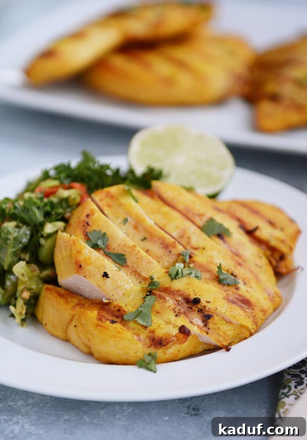 Creamy Thai Coconut Grilled Chicken 4 A white plate with sliced grilled chicken and a green salad and slice of lime on the plate.