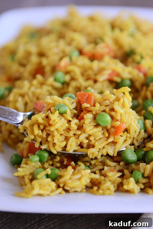 Instant Pot Indian Veggie Pulao 4 A spoon with a generous scoop of yellow-tinted Indian Vegetable Rice, showing the perfect blend of rice, peas, and carrots.