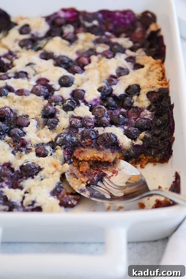 Effortless Blueberry Dump Cake 7 A large white dish of baked blueberry dump cake with a portion scooped out, revealing the golden crust and a generous amount of juicy blueberries within.