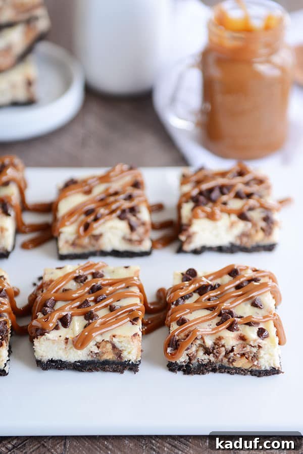 Ultimate Caramel Snickers Cheesecake Bars 3 Snickers Oreo cheesecake bars topped with chocolate chips and caramel drizzle on a white platter.