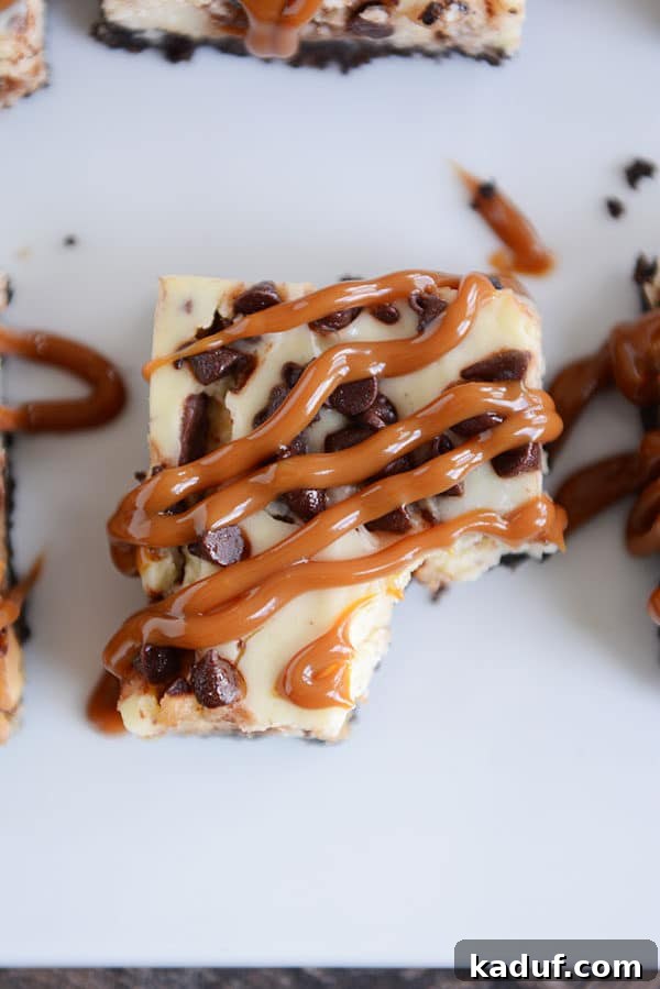 Ultimate Caramel Snickers Cheesecake Bars 4 Top view of a caramel cheesecake chocolate chip bar with a bite taken out.