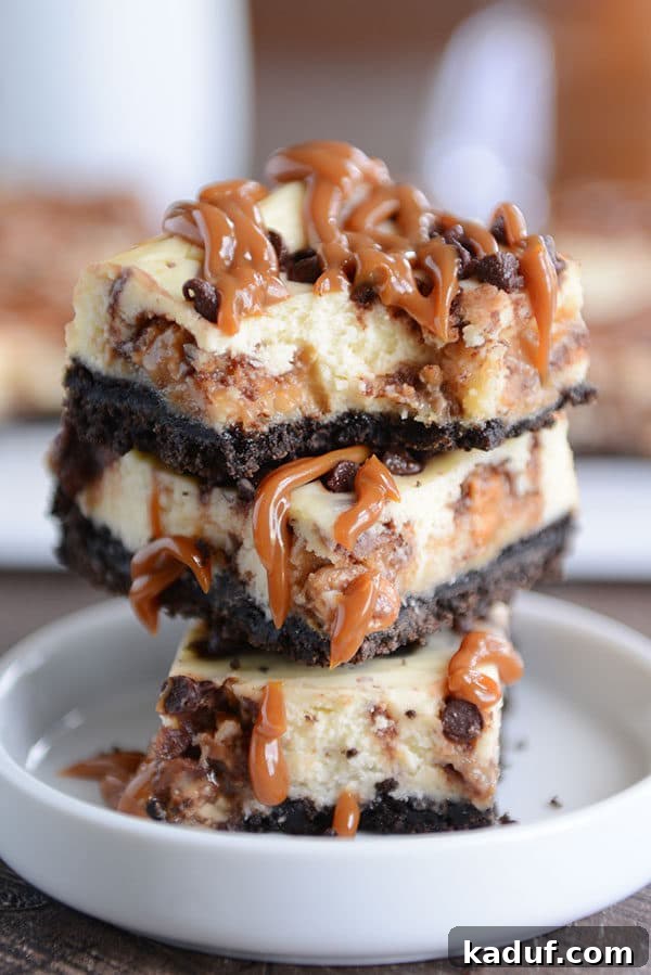 Ultimate Caramel Snickers Cheesecake Bars 5 Caramel Snickers cheesecake bars stacked on top of each other in a white ramekin.