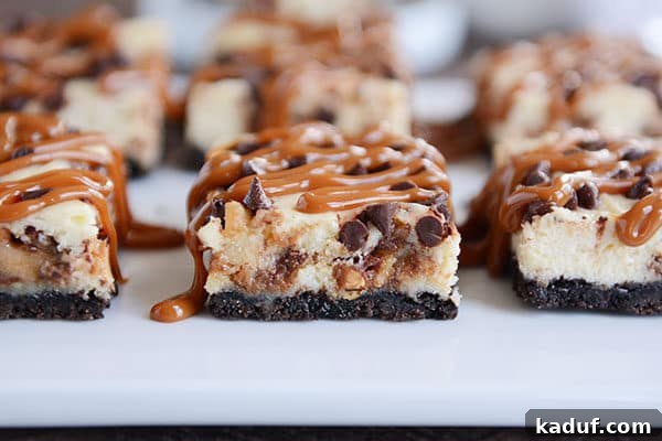 Ultimate Caramel Snickers Cheesecake Bars 7 Caramel drizzled cheesecake cookie bars on a white countertop.