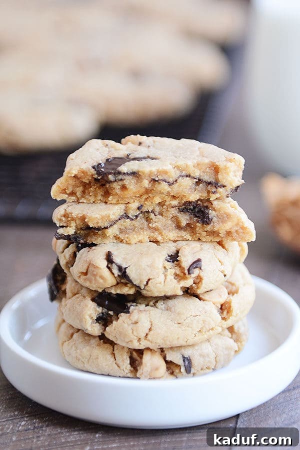 A stack of soft peanut butter chocolate chip cookies with one split in half, showcasing its fudgy interior.