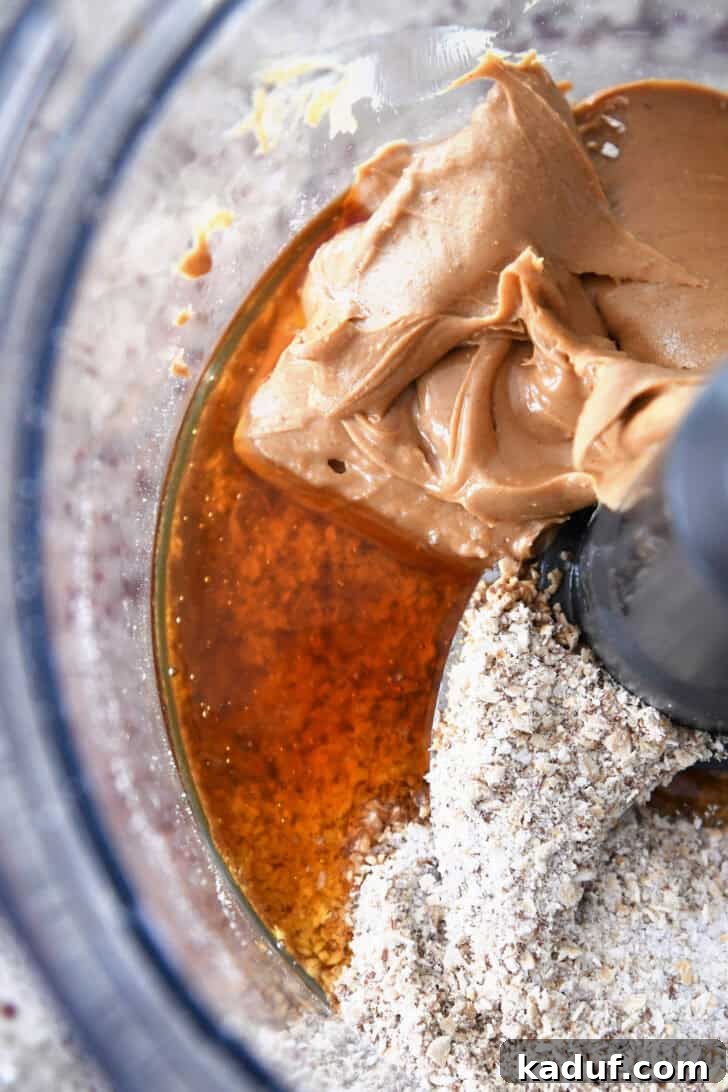 Delicious Protein Bites: Tailored to Your Taste 3 Top-down view of peanut butter, honey, and oats at the bottom of a food processor, ready for blending.