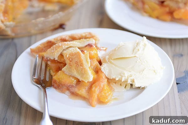 Summertime Peach Pie Perfection 9 A pristine white plate holds a delectable slice of fresh peach pie and a fork, positioned next to a melting scoop of vanilla ice cream, creating a tempting dessert scene.