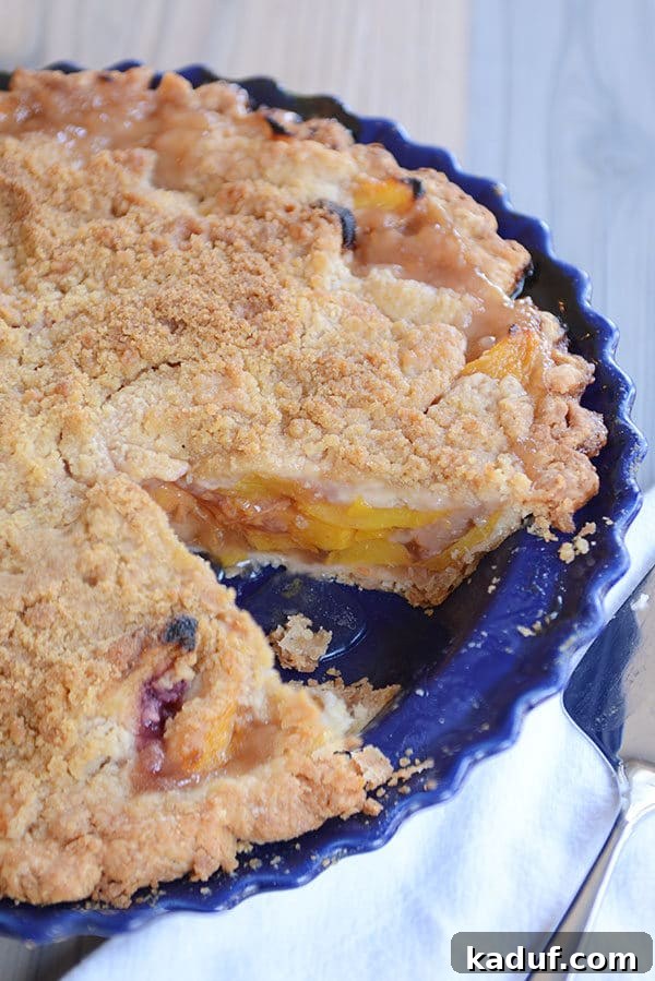 Summertime Peach Pie Perfection 5 A vibrant peach pie in a beautiful blue ceramic pie dish, with a slice already removed, revealing the abundant, tender peach filling.