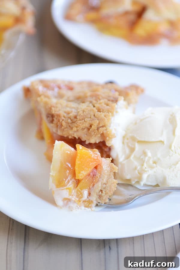 Summertime Peach Pie Perfection 6 A fork taking a generous bite out of a slice of fresh peach pie, positioned next to a melting scoop of vanilla ice cream on a clean white plate.